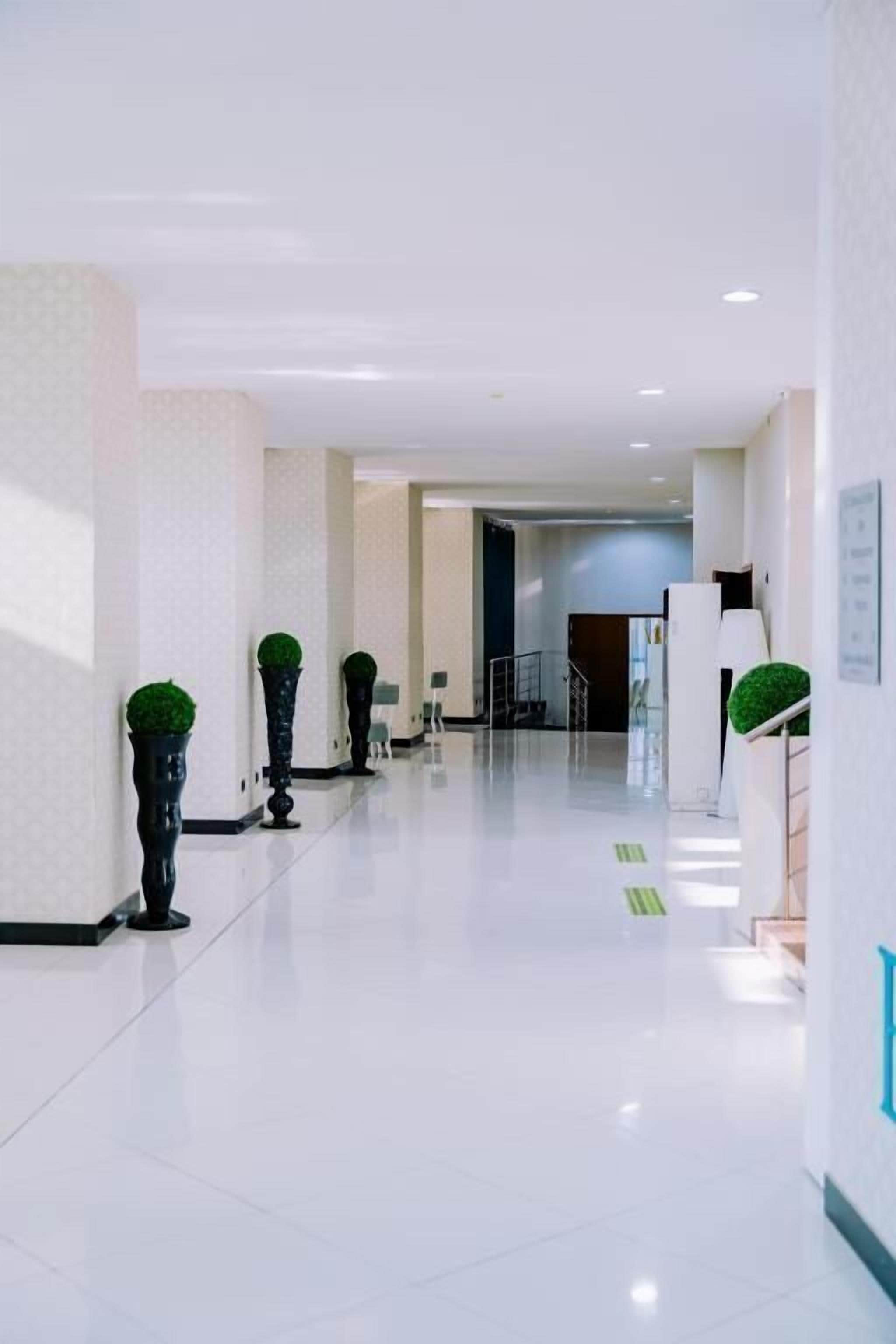 A clean, modern hotel corridor with a polished floor, potted plants, and a clear path leading to the entrance.