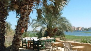An outdoor seating area with wicker furniture and a view of the water and buildings in the background. - Al Baeirat hotel (Luxor)