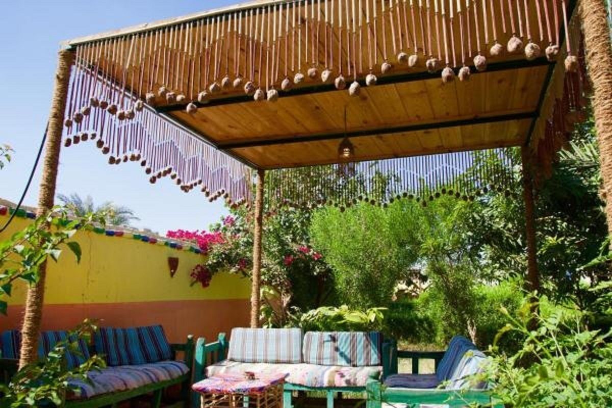 A covered outdoor seating area with striped cushions and a wooden ceiling with hanging decorations.