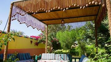 A covered outdoor seating area with striped cushions and a wooden ceiling with hanging decorations.