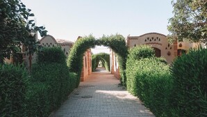 A paved pathway flanked by neatly trimmed hedges and a brick archway leading to a building. - Al Baeirat hotel (Luxor)