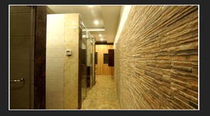A hallway with a marble wall, a wooden door, and a textured wall on the right. - Grand Krisa Resort & Spa (Manali)
