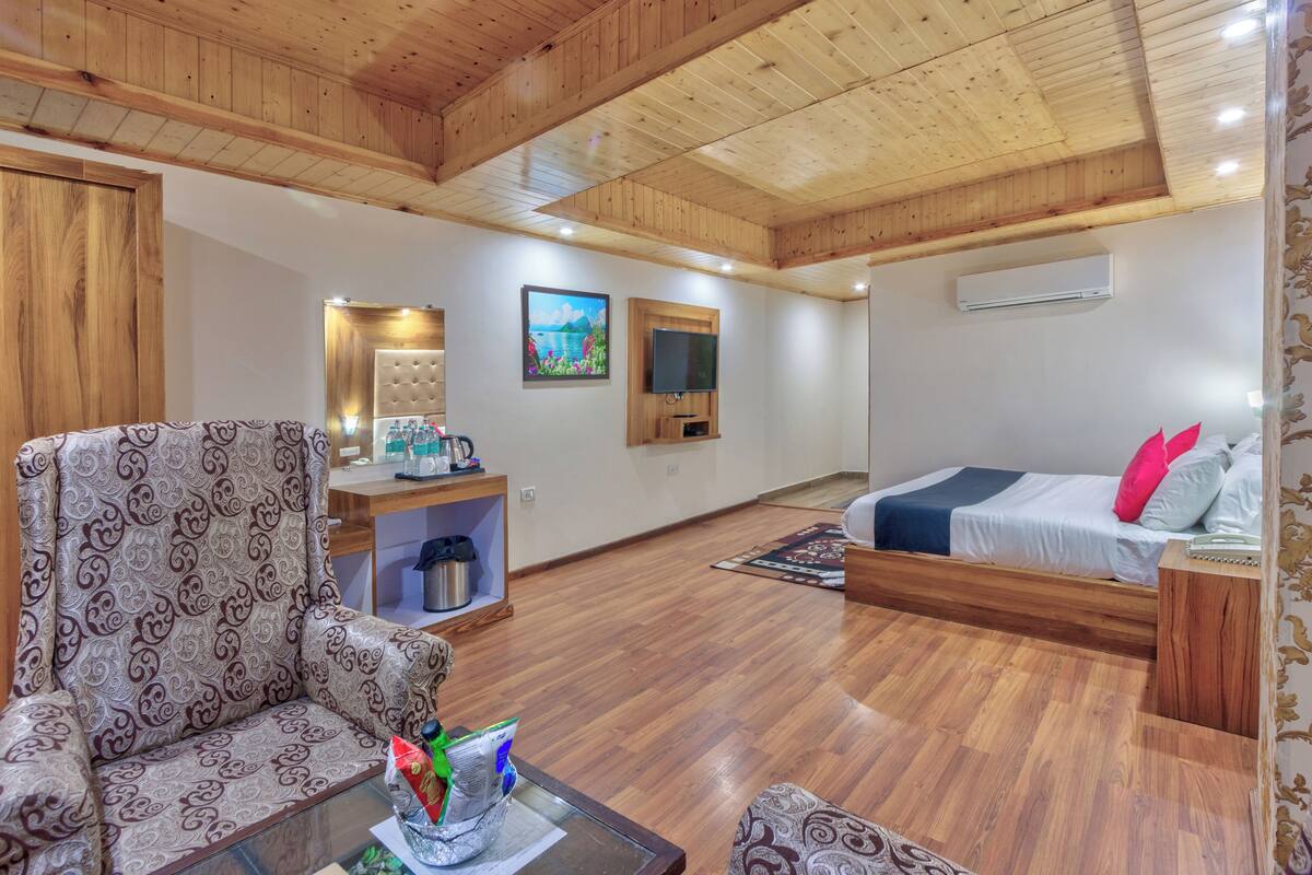 Una habitación con techo de madera, cama con almohadas, sofá, pequeña mesa con superficie de vidrio, televisor y equipo de aire acondicionado.