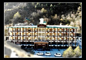 A multi-story hotel with a central entrance, balconies, and a parking area with cars. - Grand Krisa Resort & Spa (Manali)