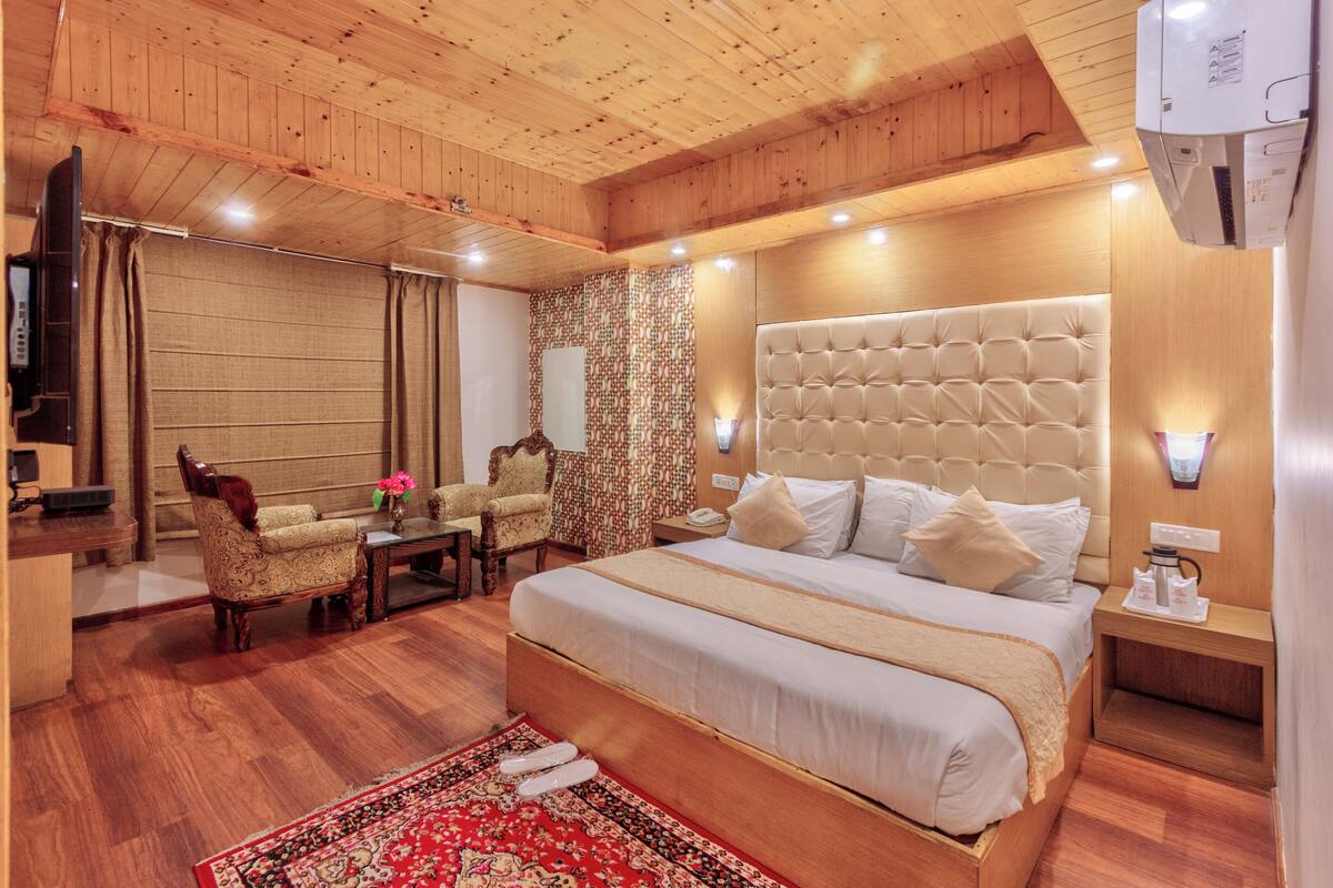 Habitación de hotel con una cama grande, techo de madera, pared con diseño, una mesita con un florero y una silla.
