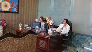 A reception desk with a computer, a vase of flowers, and a decorative statue. - Sydney Grand Hotel & Resort (New Delhi)