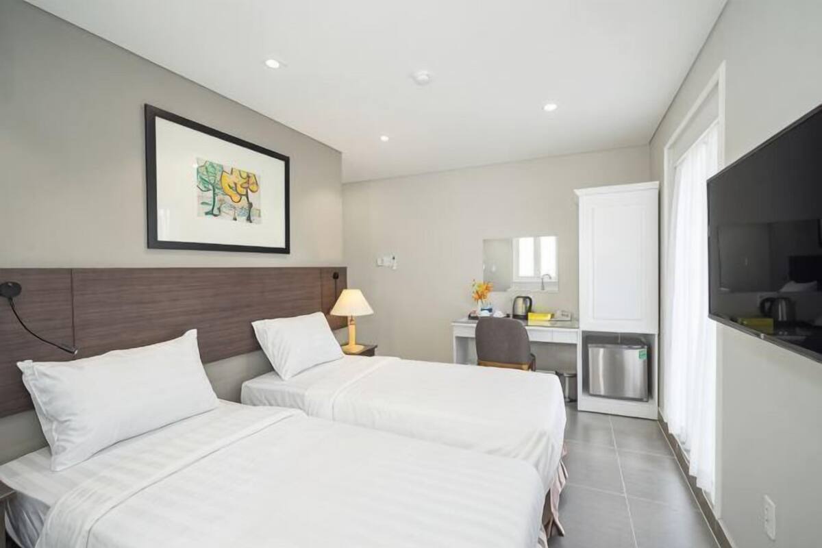 Habitación de hotel con dos camas, un escritorio, una silla, un televisor y un cuadro en la pared.