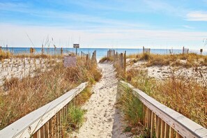 A sandy beach path with wooden railings, leading to the ocean. A sign indicates it's a private beach.