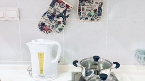 Una cocina con un hervidor blanco, una estufa y utensilios negros sobre un tapete.