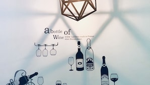 Un comedor con una mesa dispuesta para cuatro, un adhesivo mural con ilustraciones de vino y una lámpara colgante de diseño geométrico.