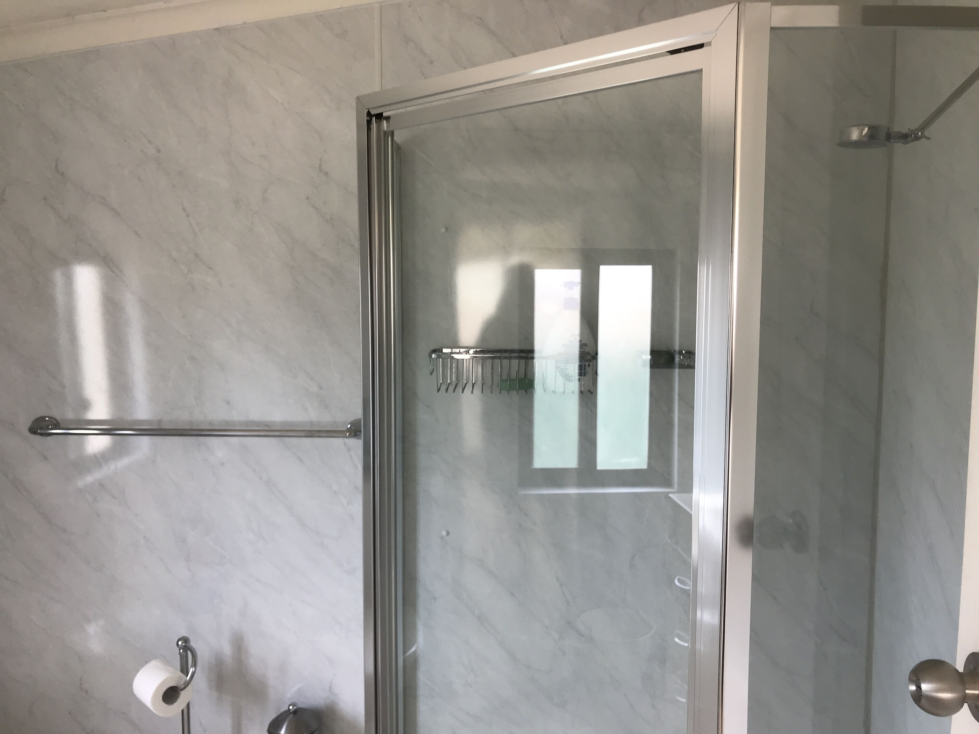 A bathroom with a glass shower enclosure, a towel rack, and a toilet paper holder.