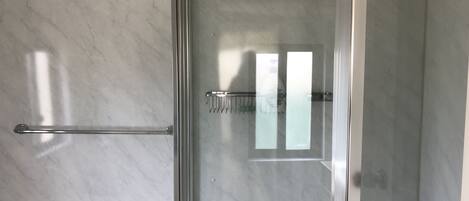 A bathroom with a glass shower enclosure, a towel rack, and a toilet paper holder.