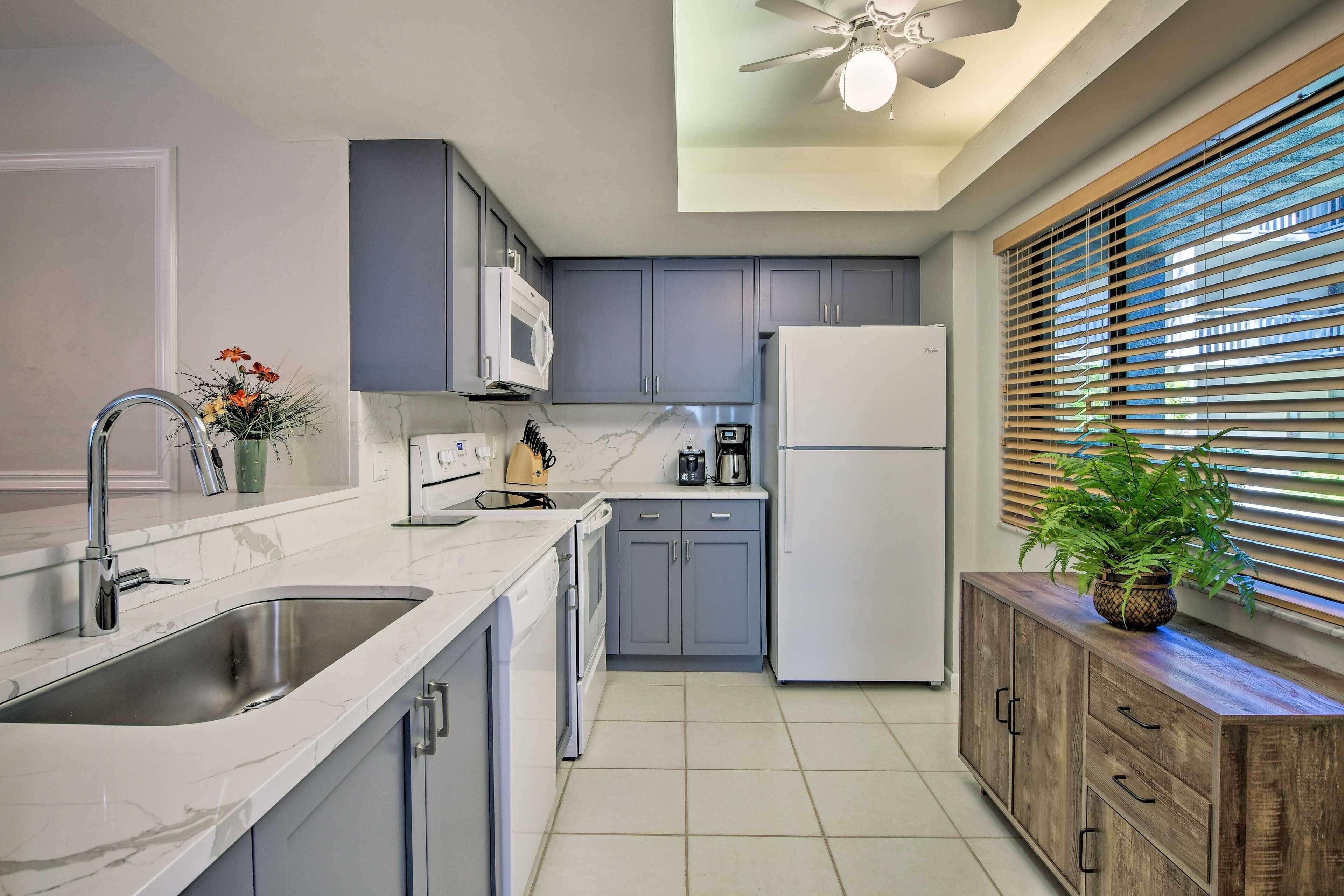 A modern kitchen with grey cabinets, a white refrigerator, and a wooden cabinet with a plant.