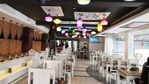 A restaurant with a long counter, white chairs, and colorful hanging lights. - Westend Inn (New Delhi)