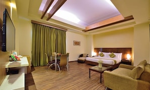 Habitación de hotel con cama, sofá, escritorio con silla, televisor y ventana con cortinas.