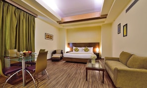 Una habitación de hotel con una mesa de vidrio, un sofá, una cama con cabecera de madera y una pequeña mesa de centro.