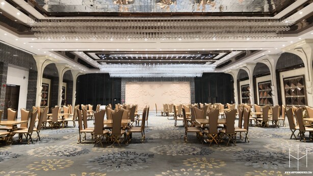 A spacious banquet hall with high ceilings, chandeliers, and rows of tables and chairs. - Westend Inn (New Delhi)