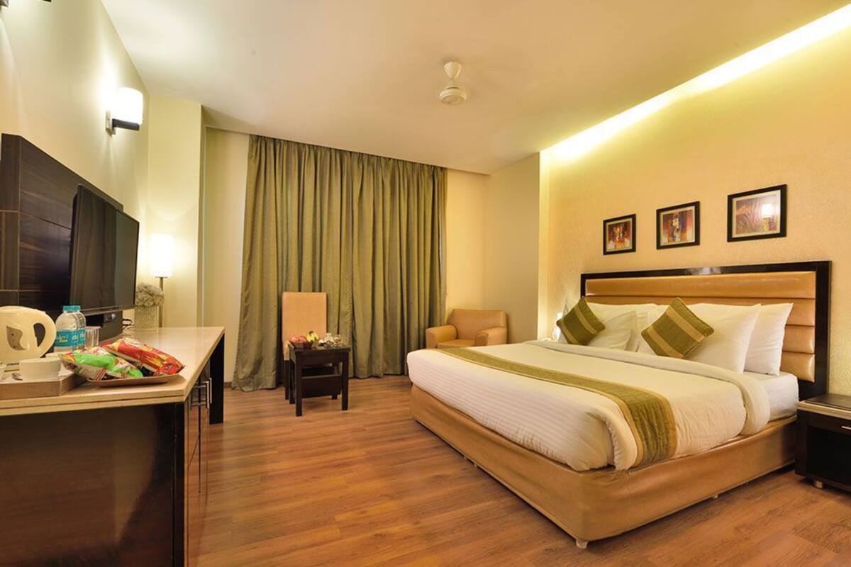 A hotel room with a bed, a desk, a chair, a TV, and a window with curtains.