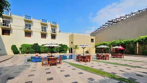 A courtyard with outdoor seating, a pool, and a building with balconies. - Westend Inn (New Delhi)