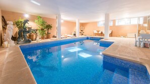 Una gran piscina interior con borde de azulejos, rodeada por una pared color beige y un techo blanco.