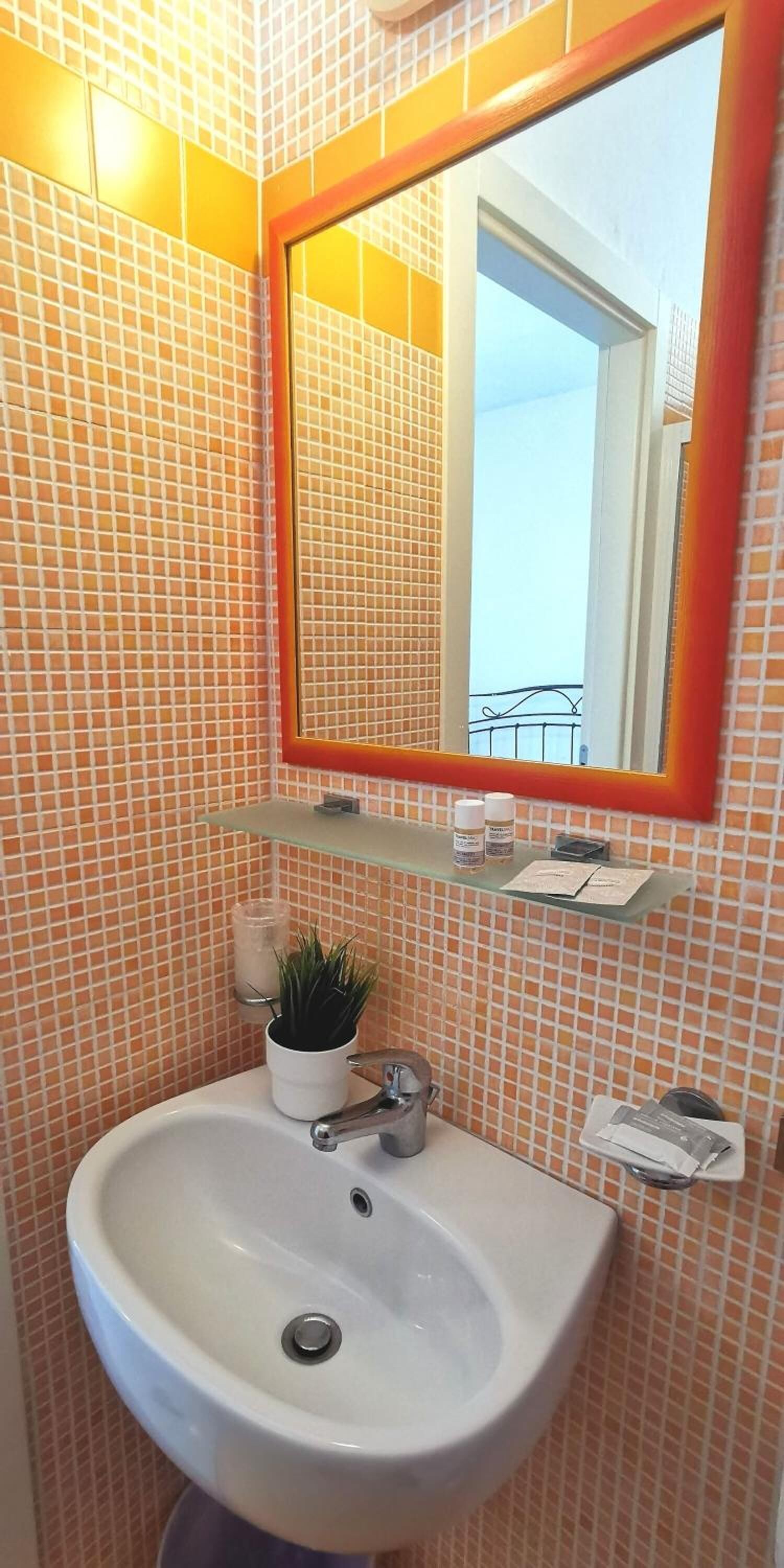 Ein Badezimmer mit einem weißen Waschbecken, einem Spiegel mit rotem Rahmen und einem kleinen Ablagebereich mit Pflegeprodukten.