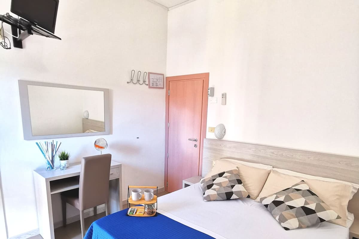 A hotel room with a bed, a desk, a chair, a TV, and a door.