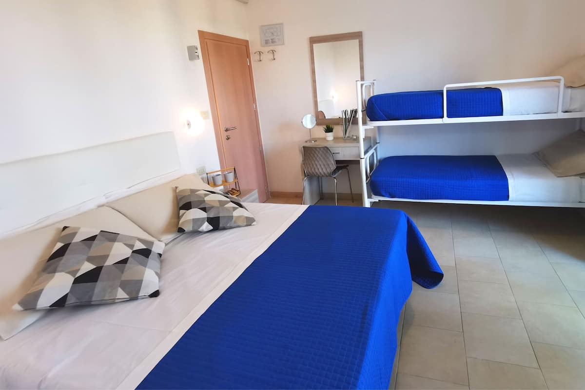 A hotel room with a single bed, a desk, a chair, and two bunk beds.