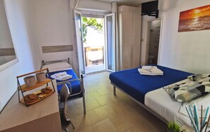 A hotel room with two beds, a desk with a chair, a window, and a view of the outside. - Hotel Bellini (Riccione)
