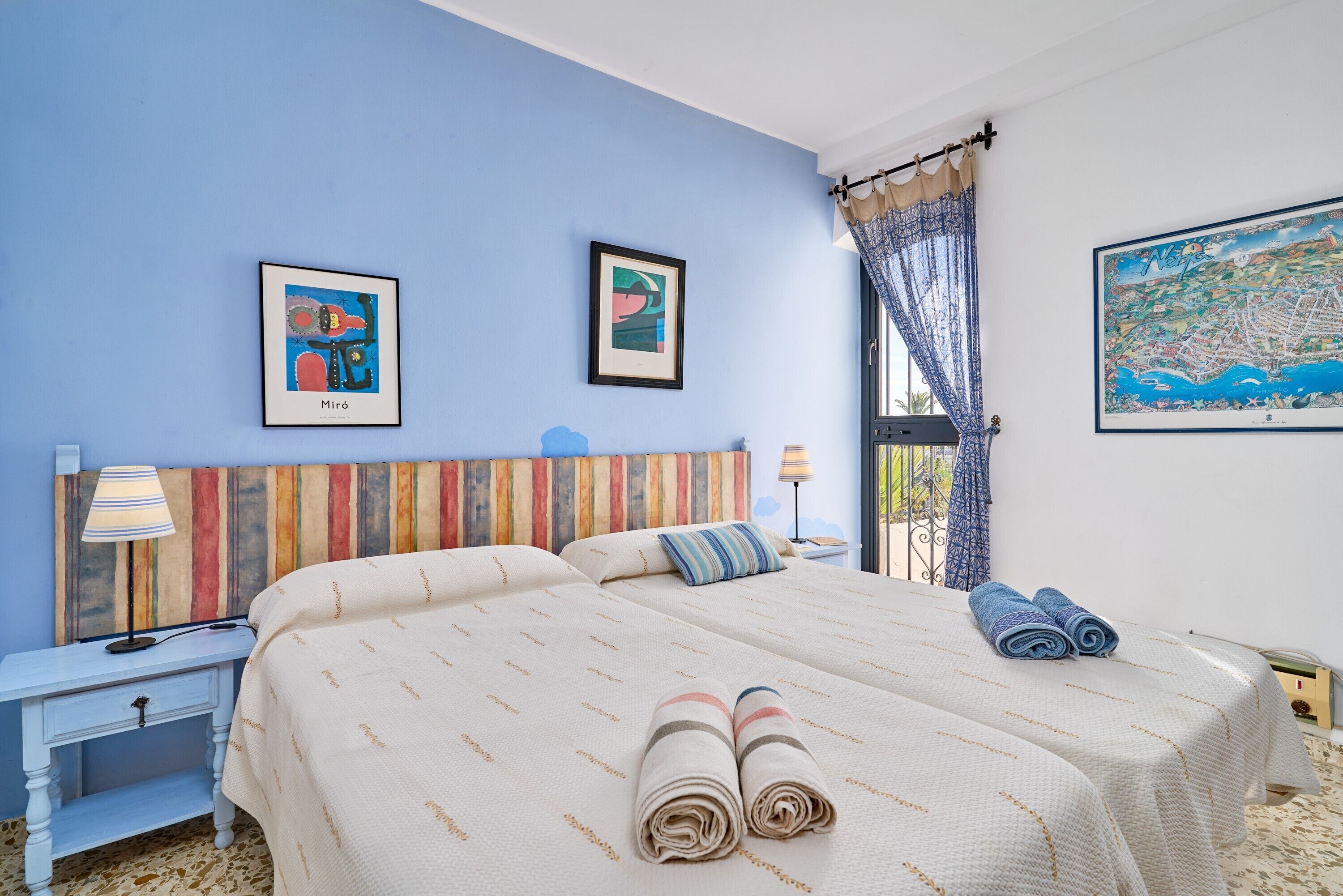A double bed with a striped headboard, two bedside tables, a lamp, and a map on the wall.