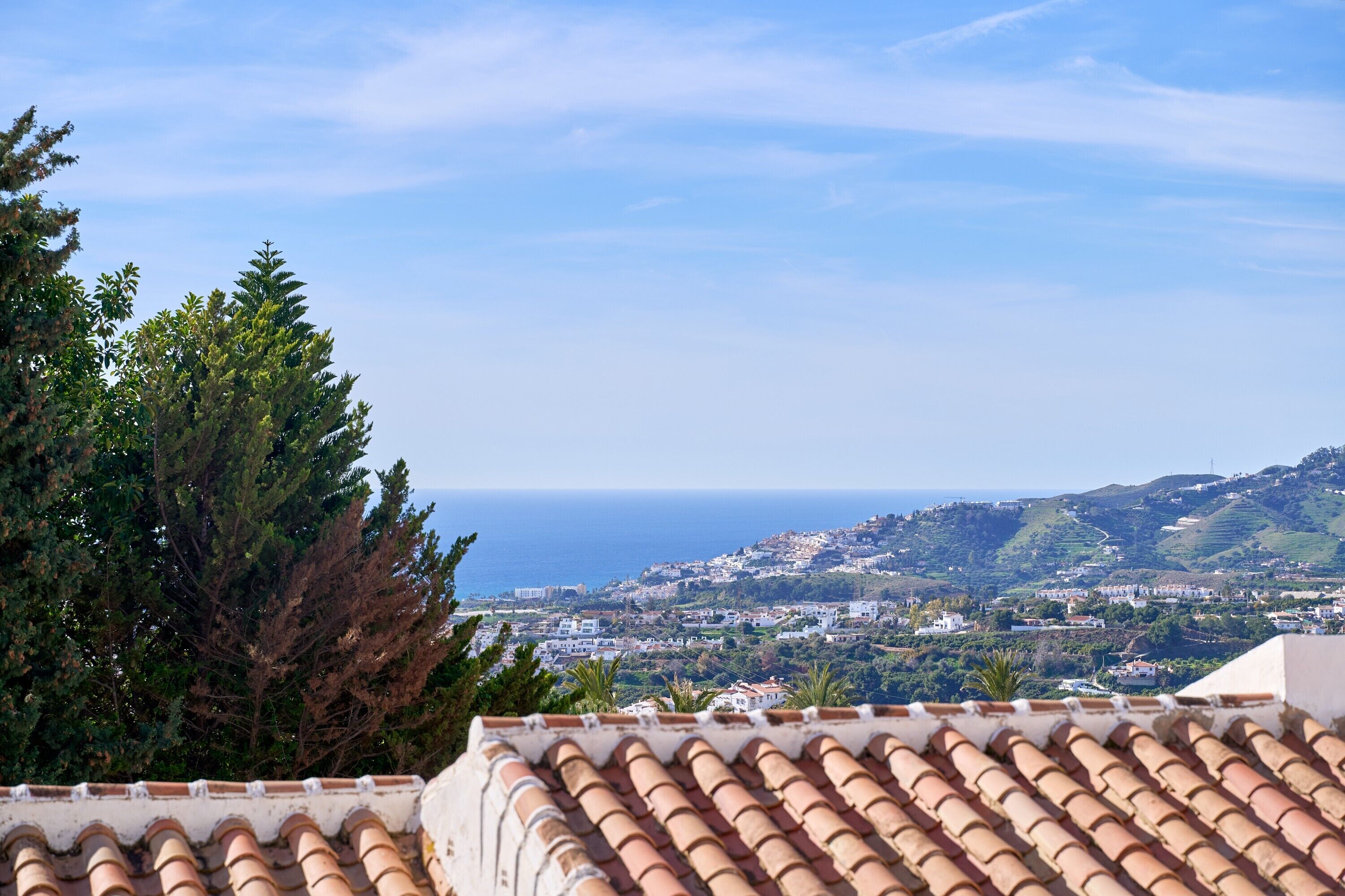 A coastal town with terracotta rooftops, dense greenery, and a view of the sea.