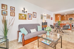 A living room with a sofa, coffee table, and wall art. There is a kitchen area visible in the background.