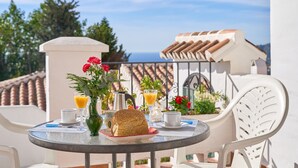 Una mesa redonda con alimentos para el desayuno, un florero con flores y vista al mar.