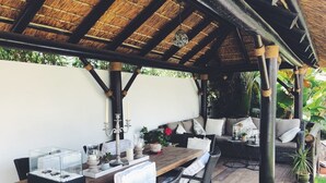 Une terrasse extérieure avec une table en bois, des chaises en osier et une structure de toit en chaume.
