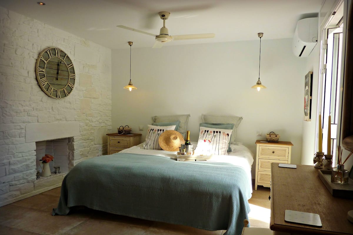 Un dormitorio con cama, mesitas de noche, un reloj, ventilador de techo y chimenea.