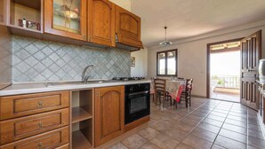 A kitchen with wooden cabinets, a stove, and a dining area with a table and chairs. - Holiday apartment surrounded by nature (Siniscola)