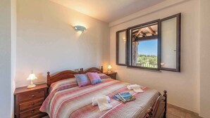 A bedroom with a bed, bedside lamps, a nightstand, a window with a view, and a wall-mounted light fixture. - Holiday apartment surrounded by nature (Siniscola)