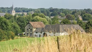 A stone building with a large arched doorway, surrounded by lush greenery and a field in the foreground. - Beautiful apartment in Simpelveld (Simpelveld)