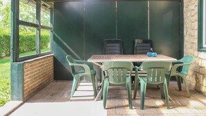 A small, enclosed patio area with a table and four chairs, a wooden ceiling, and a view of greenery outside. - Beautiful apartment in Simpelveld (Simpelveld)
