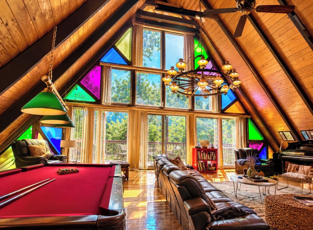 An attic room with a pool table, leather sofa, and a piano.