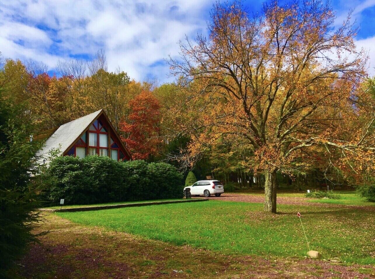 Eine Hütte mit geneigtem Dach, umgeben von einem gepflegten Rasen und verschiedenen Bäumen im Herbstlaub.