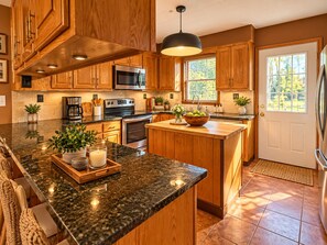 Una cocina con gabinetes de madera, encimeras de granito, electrodomésticos de acero inoxidable y un ventanal amplio.