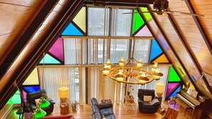 Een loft-achtige woonruimte met een schuine kap, een hoekbank, een piano en een hanglamp.