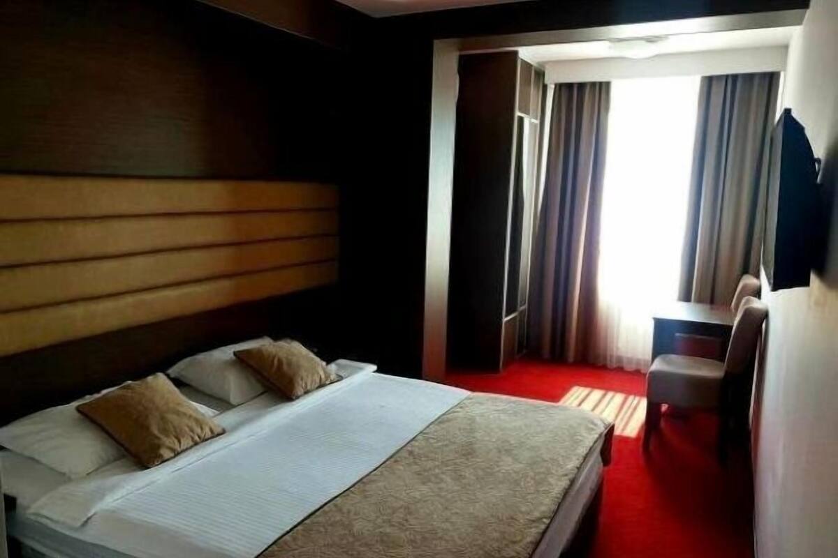 A hotel room with a bed, a desk, a chair, and a television.