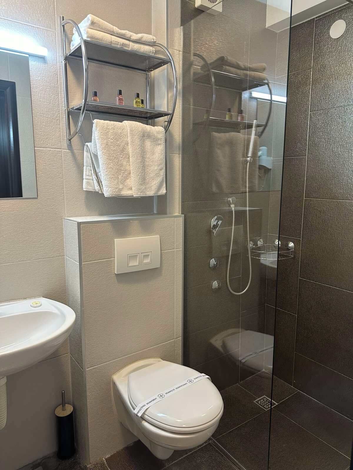 Un baño moderno con ducha envuelta en vidrio, inodoro, lavamanos y toallero con toallas.