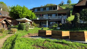 A two-story building with a balcony, surrounded by lush greenery and a clear blue sky. - Pension Schönörtli (Sigriswil)