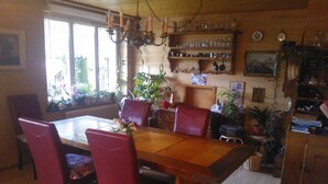 A dining room with a wooden table, red chairs, and a chandelier. There are shelves with glassware and a radiator under the windows. - Pension Schönörtli (Sigriswil)