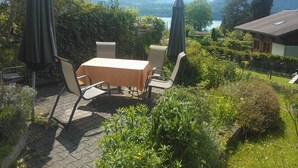 An outdoor patio with a table and chairs, surrounded by greenery and a view of mountains and a lake. - Pension Schönörtli (Sigriswil)