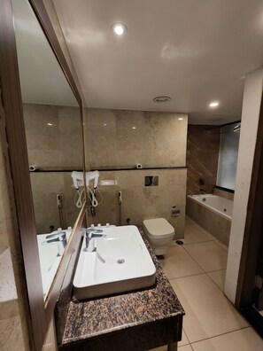 A modern bathroom with a granite countertop sink, a mirror, a toilet, a shower area, and a bathtub.