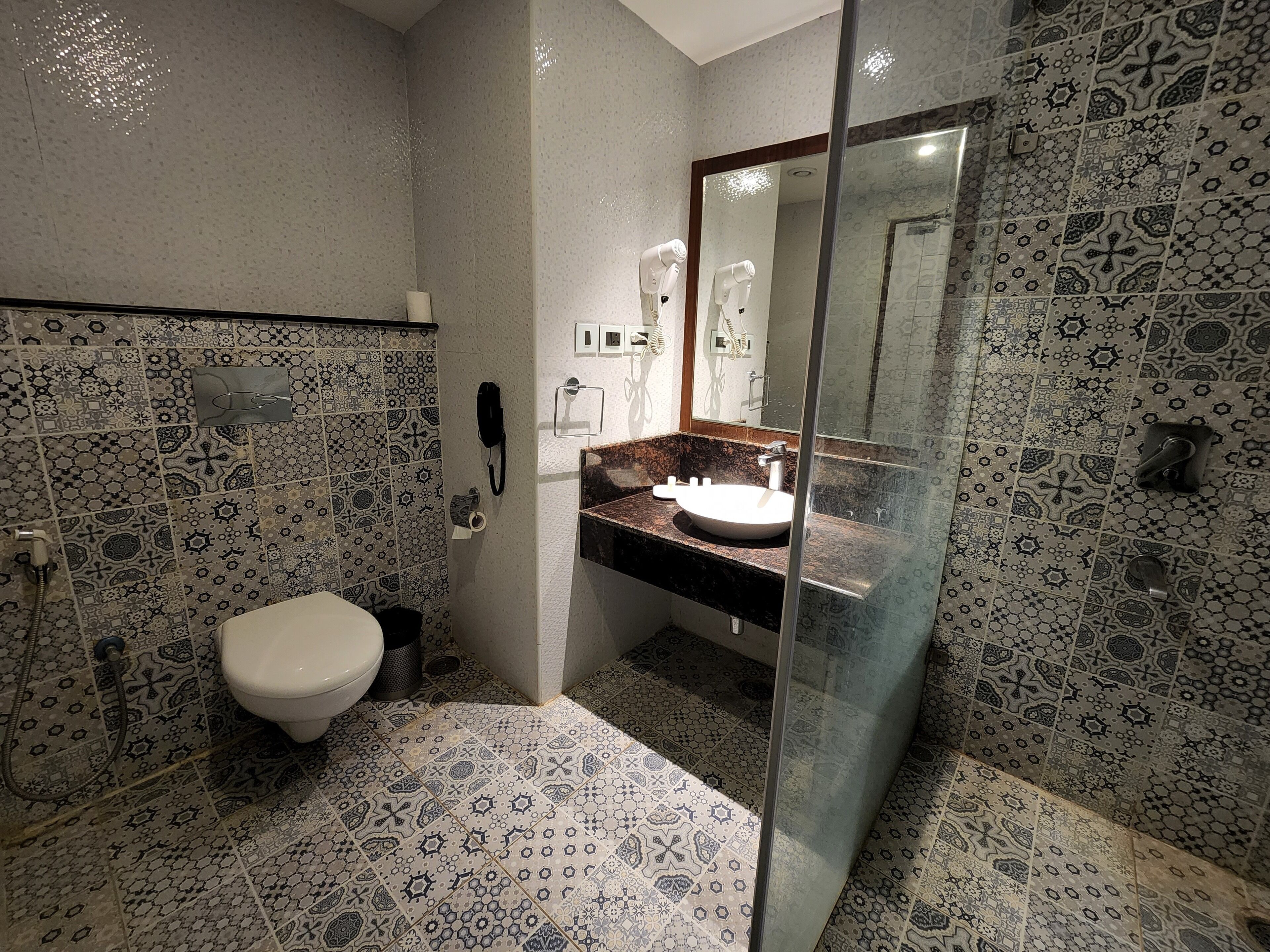 Un baño con baldosas estampadas, un inodoro, un lavabo con espejo y una cabina de ducha de cristal.