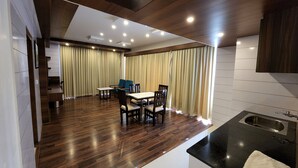 A modern kitchen with a black countertop and a sink. There is a dining area with a table and chairs. - Hotel Preethi International (Mysore)